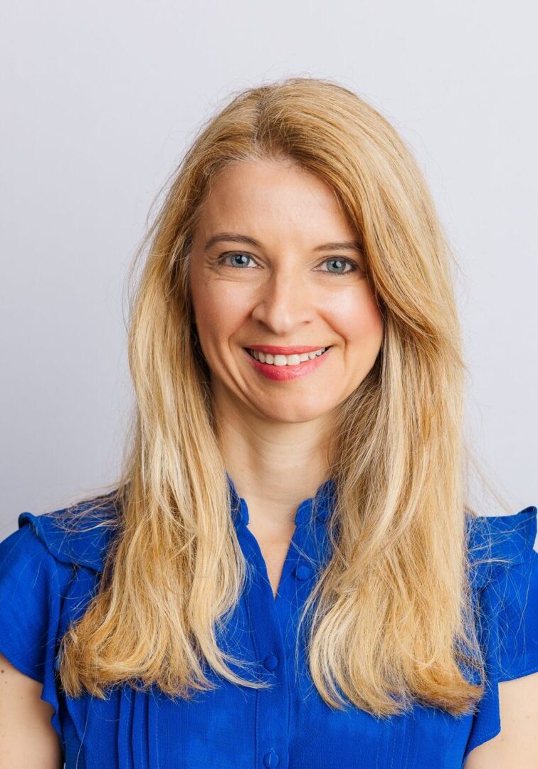 Portrait of a smiling woman with long blonde hair in a blue top.